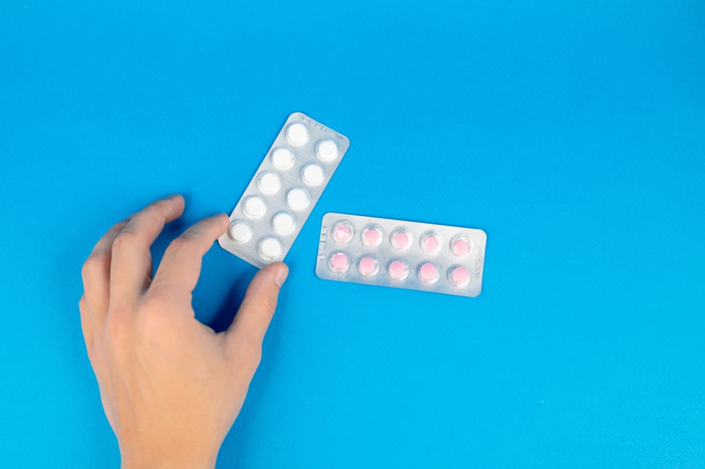 Ruka drži dva blistera s tabletama protiv bolova na plavoj podlozi