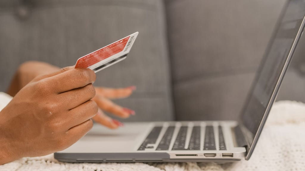 Osoba drži bankovnu karticu ispred prijenosnog računala tijekom kupnje na internetu